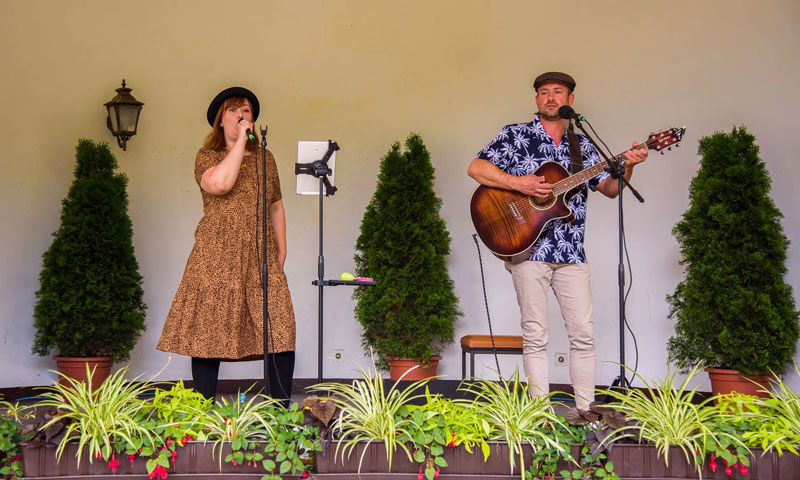 Jana und Danny auf einer mit Pflanzen dekorierten Bühne mit Mikrofonen und Gitarre