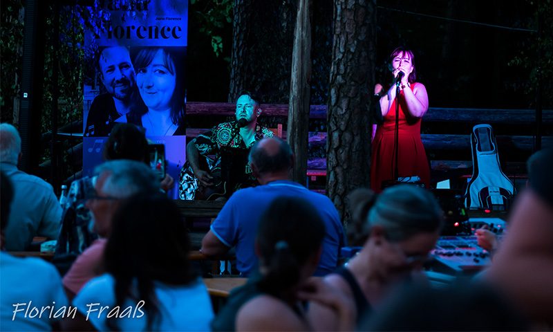 Jana und Danny mit Gitarre vor eigenem Jana Florence Roll-Up in blauem Licht singend vor einem Publikum